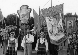 Melnbalta bilde no izstādes "Dziesmu spēks" - kadrs no gājiena, karogi un Dziesmu svētku karogs, kolonnas sākums