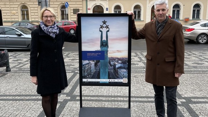 Sievietis un vīrietis pie plakāta ar brīvības pieminekļa attēlu