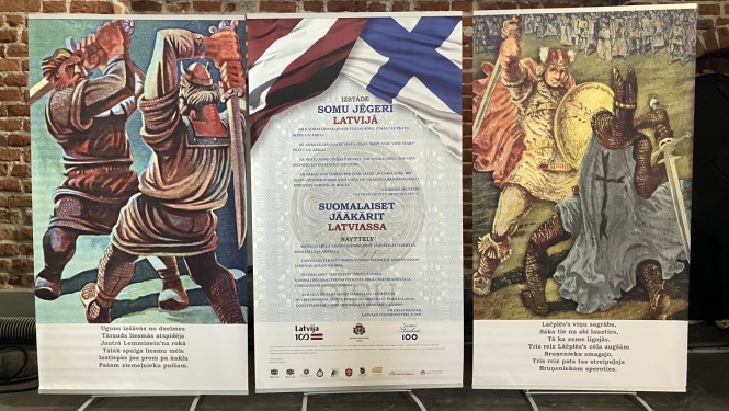 Krāsaina bilde, izstādes atklāšanas stendi, pa kreisi ilustrācija no Somu eposa Kelevala, pa labi - no Lāčplēša