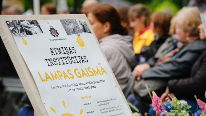 pasākuma baneris, fonā cilvēki