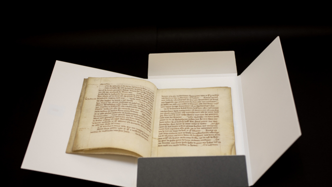 Krāsaina bilde, dokumentu mapē ievietots atvērts 13.gadsimta dokuments, tā nosaukums - Nogorodas kantora noteikumi jeb šrāgas 1295. gada redakcijā