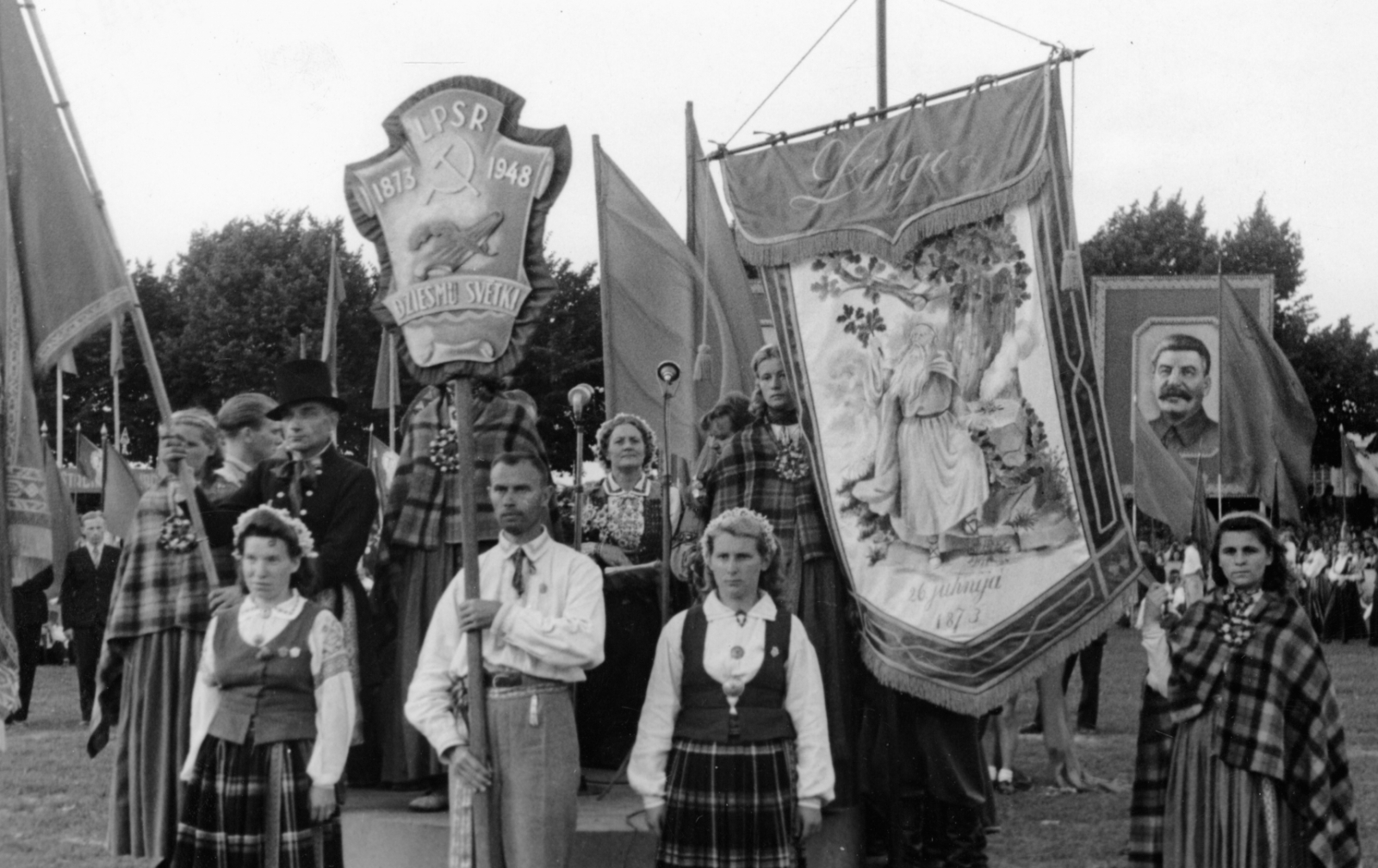 Melnbalta bilde no izstādes "Dziesmu spēks" - kadrs no gājiena, karogi un Dziesmu svētku karogs, kolonnas sākums