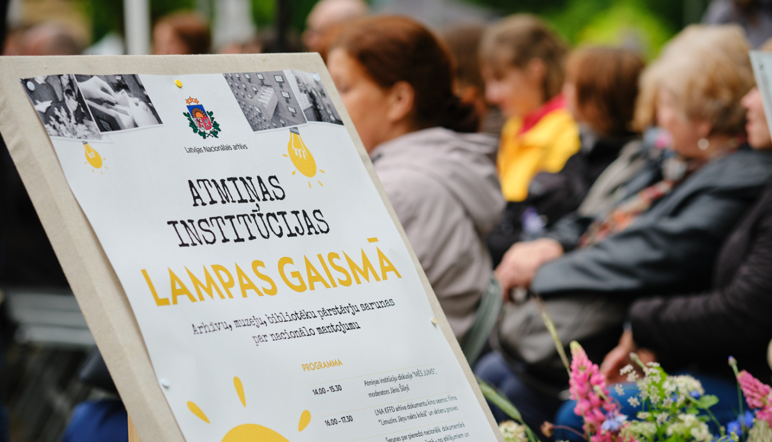 pasākuma baneris, fonā cilvēki