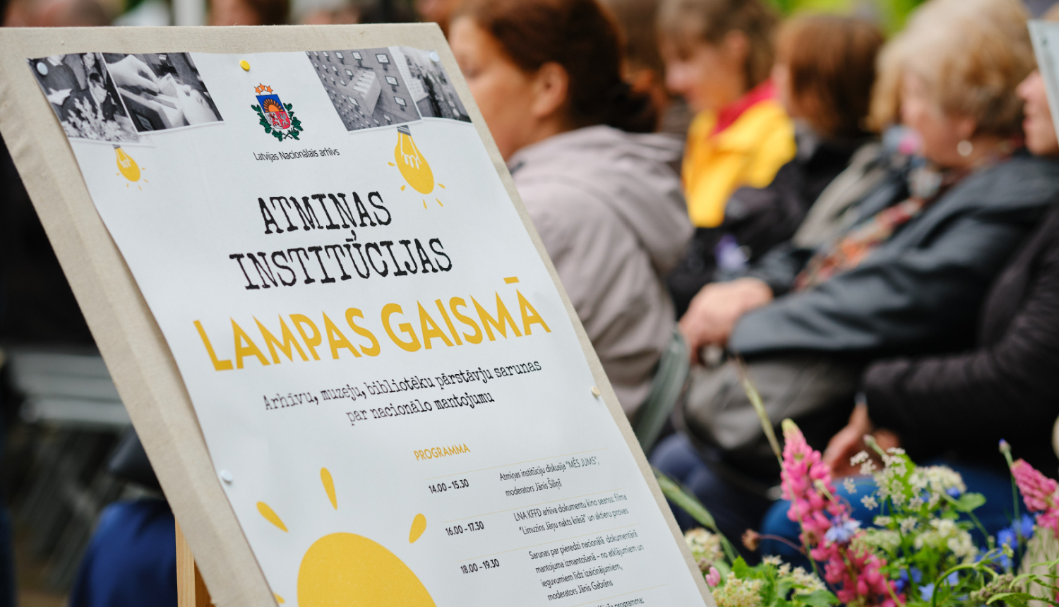 pasākuma baneris, fonā cilvēki